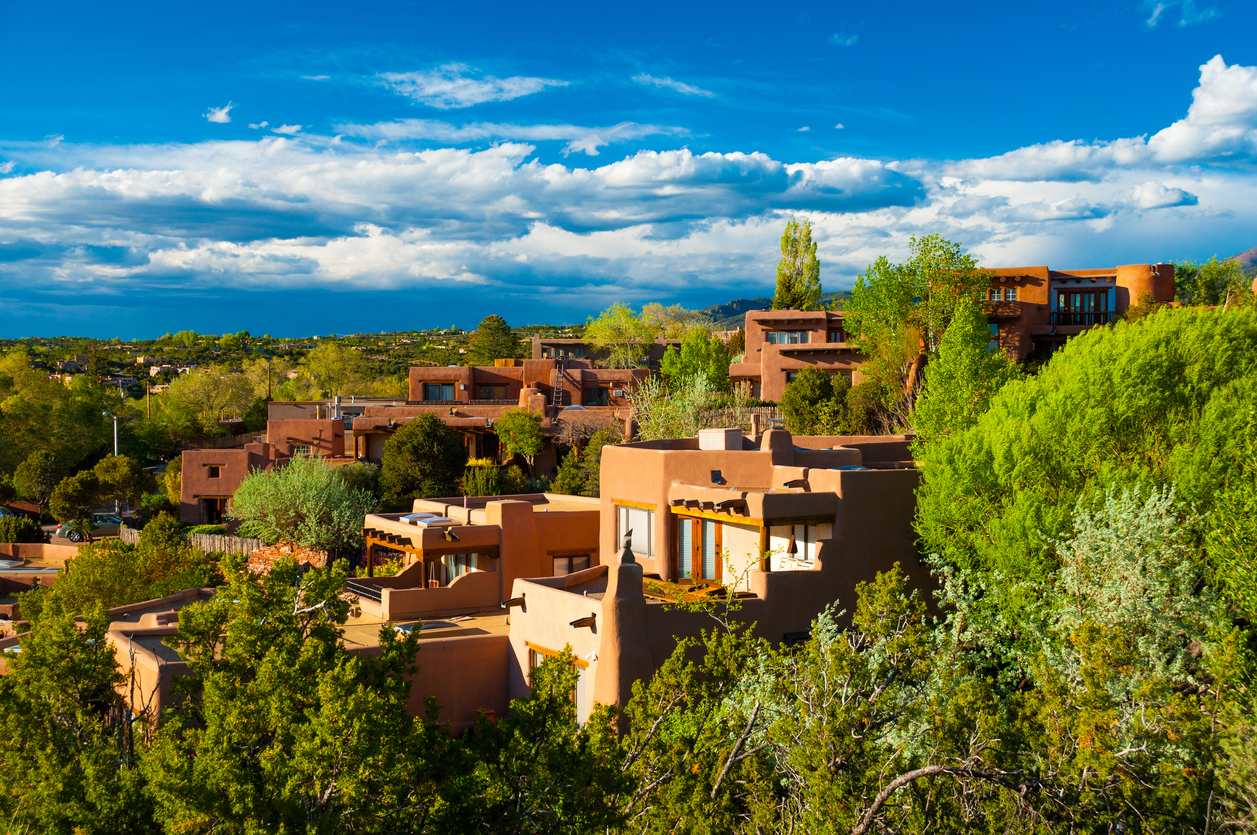 Hillside houses and trees in Santa Fe, New Mexico, with clouds in the background.